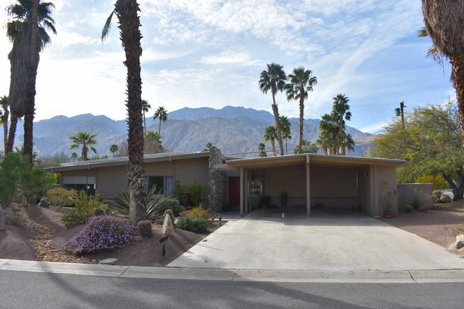 Orchid Tree’s low roofline and stacked stone beneath palms, with the San Jacinto Mountains behind the house